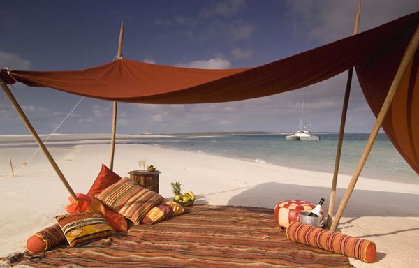 Beach picnic beneath traditional sails with cushions