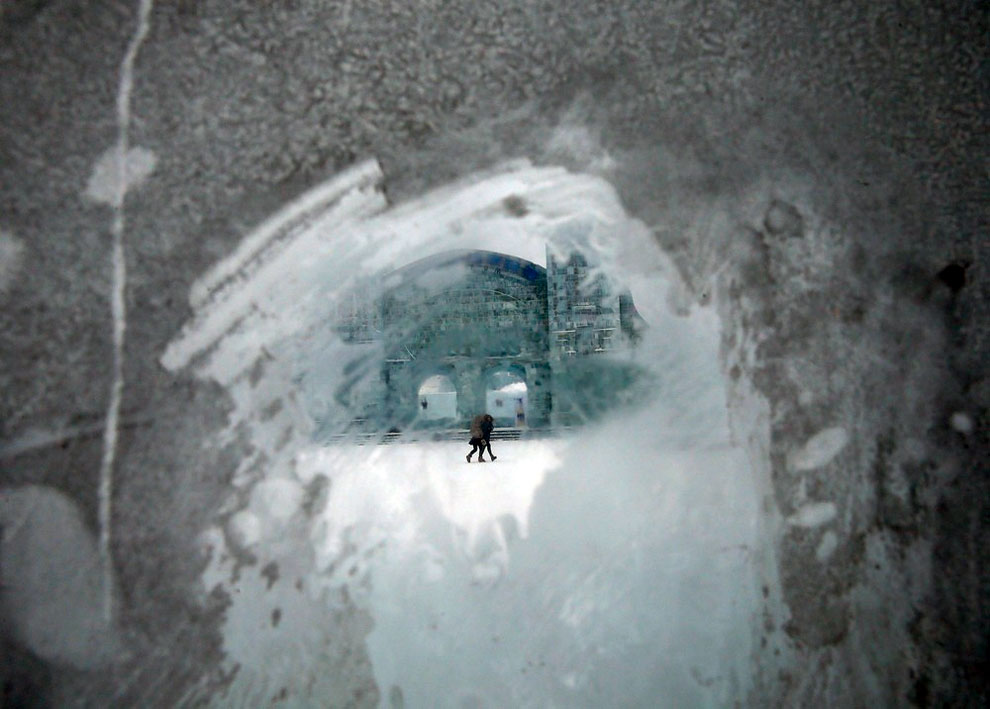 Visitors walking past an ice sculpture are seen through a frozen window 