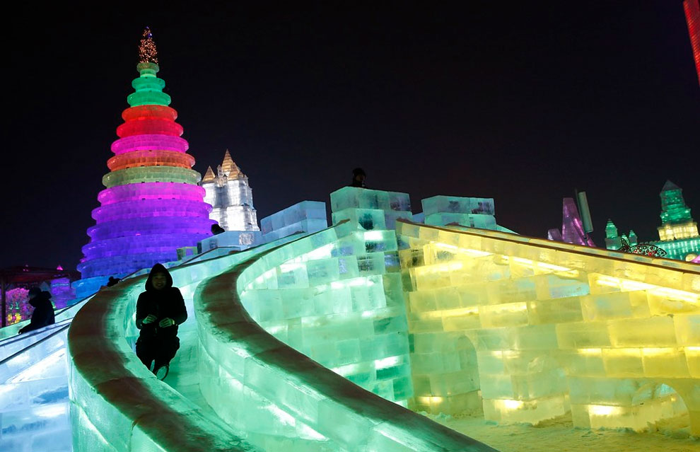 A man rides a slide on an ice sculpture illuminated by colored lights during a trial operation 