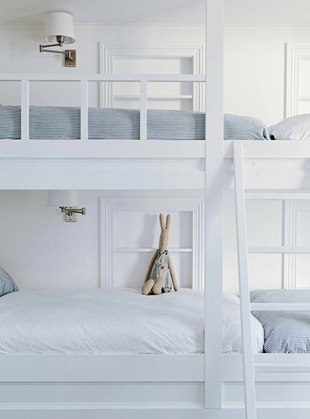 Bunk beds are great space savers, and a crisp, all-white color scheme will make a small room feel spacious and calming. Here, linen in the blue-ticking fabric adds subdued color, while extendable wall lamps add another layer of functionality.